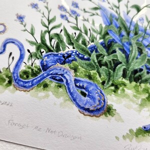 K&ouml;nnte beinhalten: Aquarellmalerei eines blauen Drachen, der sich in einem Bett aus Vergissmeinnicht-Blumen zusammenrollt. Der Drache hat goldene Akzente und ist von gr&uuml;nen Bl&auml;ttern umgeben. Das Gem&auml;lde ist mit "Juli 2021" signiert und tr&auml;gt den Titel "Vergissmeinnicht-Drache".