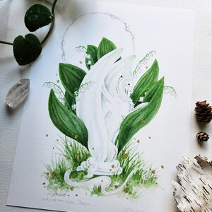 Puede incluir: Ilustraci&oacute;n en acuarela de un drag&oacute;n blanco emergiendo de hojas verdes y flores de lirios del valle. El drag&oacute;n tiene detalles intrincados y est&aacute; rodeado por un halo. La obra est&aacute; firmada y titulada "Lily-of-the-Valley Dragon".