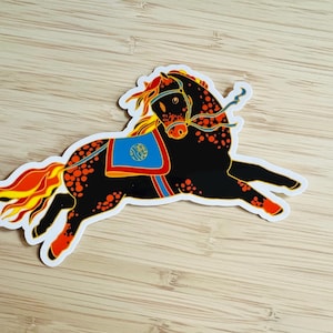 May include: A sticker featuring a black horse in a running pose, adorned with orange spots and accents. The horse has a blue saddle with a gold emblem and a flowing mane and tail in shades of orange and yellow. A blue rein is visible.