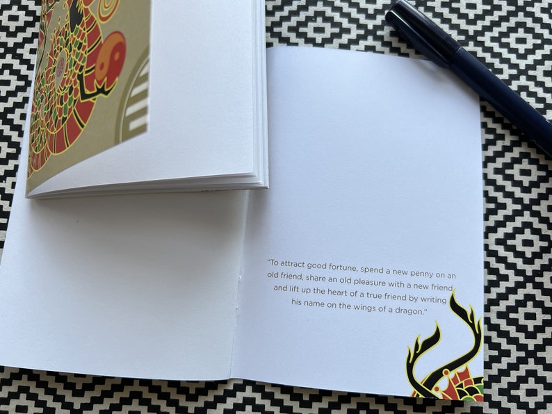 May include: A small, white book with a gold and red dragon design on the cover. The book has a quote on the inside page that reads: "To attract good fortune, spend a new penny on an old friend, share an old pleasure with a new friend and lift up the heart of a true friend by writing his name on the wings of a dragon."