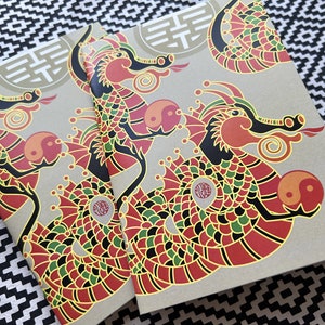 May include: Two brown notebooks with a red, green, black, and yellow dragon design. The dragon is holding a yin yang symbol. The notebooks have a gold double happiness symbol on the cover.