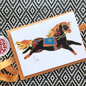 May include: A greeting card featuring a black and orange horse with a red, blue, and gold saddle. The horse is running with its mane and tail flowing. The card has the word "HORSE" written in black at the bottom.