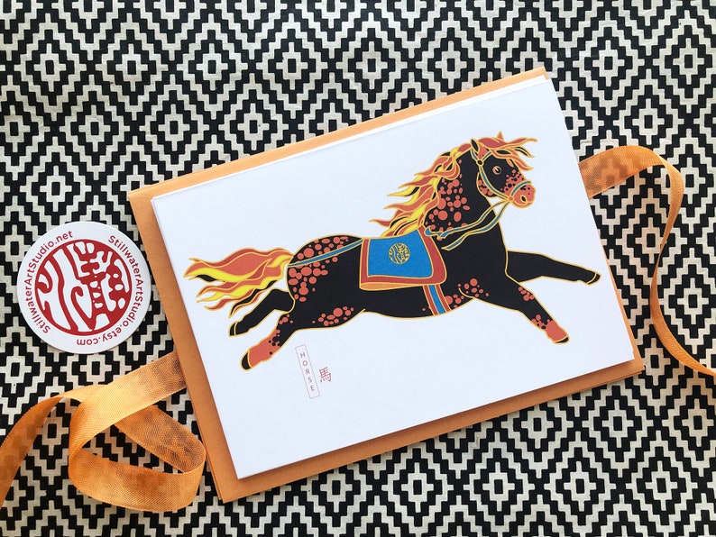 May include: A greeting card featuring a black and orange horse with a red, blue, and gold saddle. The horse is running with its mane and tail flowing. The card has the word "HORSE" written in black at the bottom.