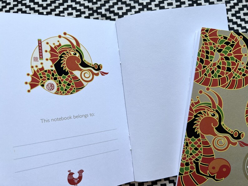 May include: A red, green, and gold dragon illustration on a white notebook cover. The dragon is holding a yin yang symbol. The text "This notebook belongs to:" is printed below the illustration.