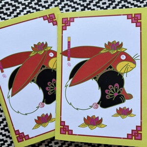May include: Two yellow cards with red and black rabbits wearing flower crowns. The cards have the Chinese character for rabbit and the word "rabbit" written vertically on them.