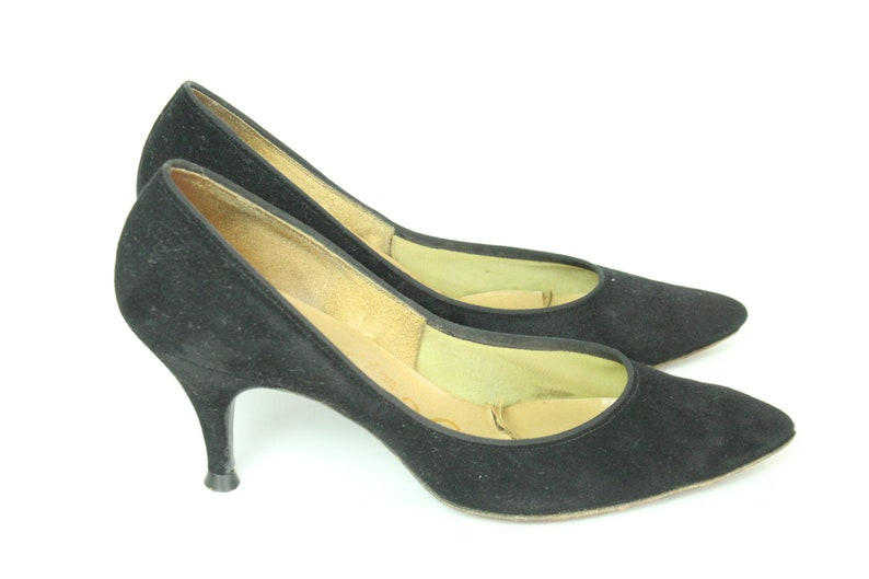 May include: A pair of black suede pumps with stiletto heels. The shoes have a pointed toe and a closed design.