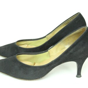 May include: A pair of black suede high heels with a pointed toe and a stiletto heel.