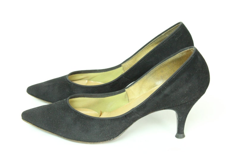 May include: A pair of black suede high heels with a pointed toe and a stiletto heel.