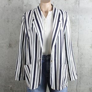 May include: A navy and white striped blazer with two front pockets and gold buttons. The blazer is worn over a white collared shirt and blue jeans. The jacket has a classic, tailored design.