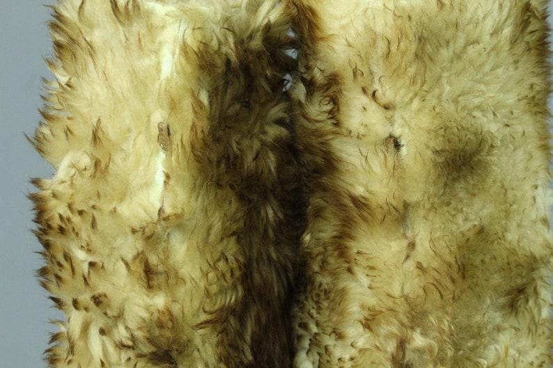 May include: Two pieces of sheepskin with a light brown and white color. The sheepskin has a soft, fluffy texture.