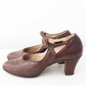 May include: A pair of brown leather heeled shoes with a strap and buckle detail. The shoes have a pointed toe and a low heel.