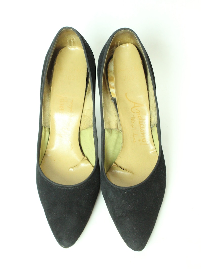 May include: A pair of black suede high heels with a pointed toe. The shoes have a light brown leather insole with the text "J. Adamy! Made in Italy" printed on the insole.