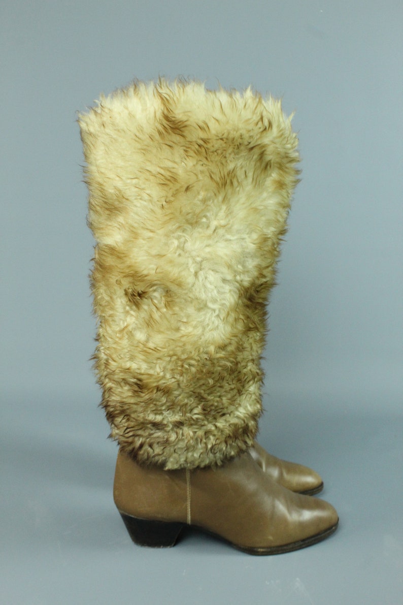 May include: A pair of brown leather knee-high boots with a faux fur cuff. The boots have a pointed toe and a low block heel.