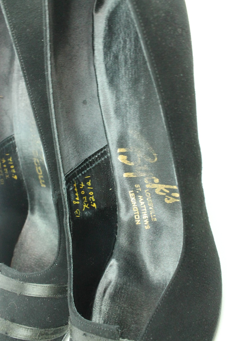 Op de afbeelding: Zwarte su&egrave;de schoenen met een gouden inscriptie die "Prick's Louisville, St. Matthews, Lexington 620121 13 8000 7120 &euro;20/21" luidt.