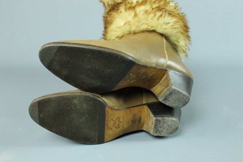 May include: Brown leather boots with a fur cuff. The boots have a wooden heel and a rubber sole.