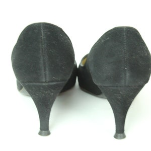 May include: A pair of black suede heeled shoes with a pointed toe. The shoes are shown from the back, with the heels facing the viewer.