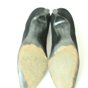 May include: A pair of black suede heeled shoes with worn soles. The shoes have a pointed toe and a high heel.