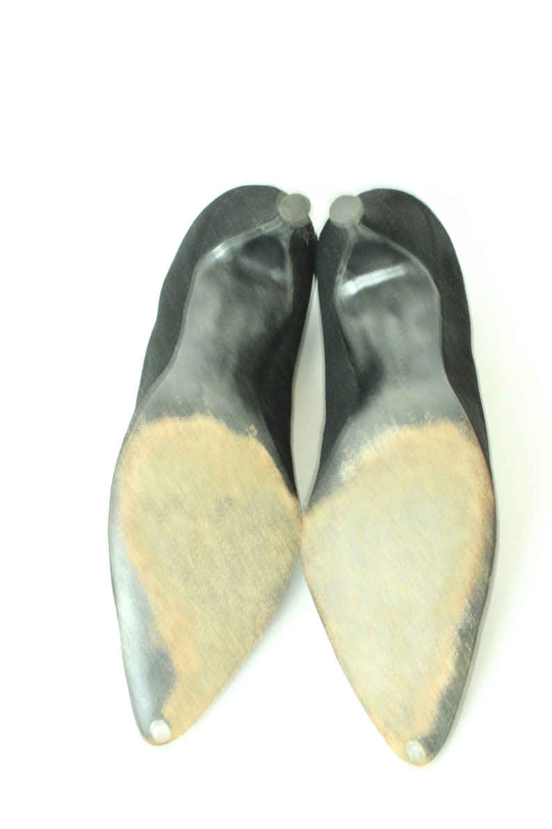 May include: A pair of black suede heeled shoes with worn soles. The shoes have a pointed toe and a high heel.