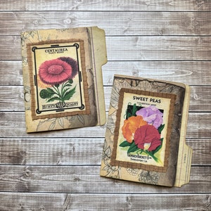 May include: Two vintage-style seed packets, one for Centaurea Fancy Mixed and the other for Sweet Peas Cuthbertson Mixed. Both packets feature colorful flower illustrations and are framed with brown paper and decorative borders.
