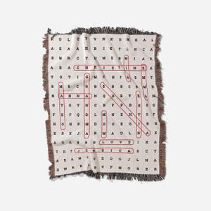 May include: A beige woven throw blanket with a red word search puzzle featuring the words "CHRISTIAN", "LOVE", and "JESUS".