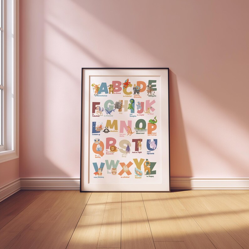 May include: A framed alphabet poster with colorful illustrations of animals and objects for each letter. The poster is in a black frame and is displayed on a wooden floor against a pink wall. The alphabet is in uppercase letters.