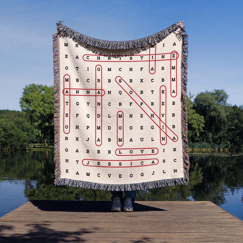 May include: A woven throw blanket with a cream background and red lettering. The blanket features a word search puzzle with the words "CHRISTINE", "LOVE", and "JESSICA" spelled out.