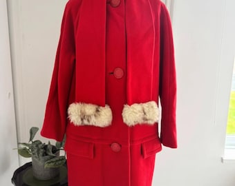 Puede incluir: Un abrigo de lana rojo vintage con una bufanda a juego y puños de piel. El abrigo tiene botones rojos grandes y dos bolsillos delanteros. El abrigo se exhibe en un maniquí en una habitación bien iluminada.