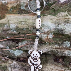 May include: White bear charm keychain with black and white beads and a silver key ring. The bear charm is carved with a smiling face and a guitar.
