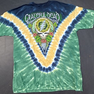 May include: A tie-dye t-shirt with a green, blue and yellow colour scheme. The shirt features a Grateful Dead logo with a skull and lightning bolt design.