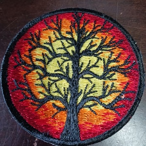 Peut inclure: Patch brodé représentant un arbre de vie noir sur fond de coucher de soleil rouge, orange et jaune.