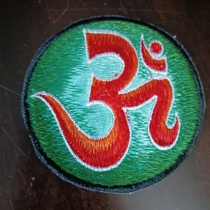 Könnte beinhalten: Ein gestickter Patch in Grün und Rot mit dem Symbol Om in einem Kreis.
