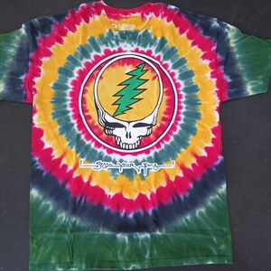 May include: Tie-dye t-shirt with a circular design in shades of green, yellow, red, and blue. The shirt features a skull with a lightning bolt on the front, with the text "Steal Your Face!" below the graphic.