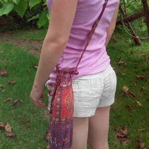 May include: A woman wearing a pink tank top and white shorts is carrying a colorful drawstring bag with a long strap.