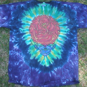 May include: A tie-dye t-shirt with a colorful graphic of a rose and a butterfly. The rose is red, yellow, and green, and the butterfly is blue and purple. The shirt is a dark blue color with a tie-dye pattern.