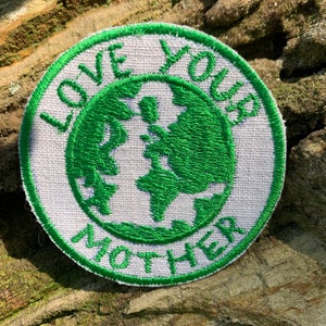 May include: A white and green embroidered patch with the text "Love You Mother" and a green outline of the Earth in the centre.