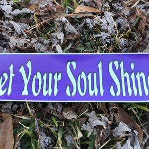 Puede incluir: Una pegatina rectangular morada con las palabras "Let Your Soul Shine" en letras blancas estilizadas. La pegatina se encuentra sobre un fondo de hojas secas y hierba.