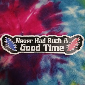 May include: A black and white sticker with the text "Never Had Such A Good Time". The sticker has blue and red lightning bolt designs on each side. The background is a tie-dye pattern in shades of pink, blue, and purple.