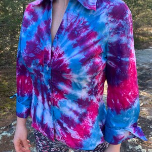 Op de afbeelding: Een blauw, roze en wit tie-dye overhemd met lange mouwen. Het shirt heeft een draaiende print.