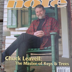 Puede incluir: Portada de la revista "Hittin' the Note" con Chuck Leavell. La portada muestra a un hombre con una camisa a cuadros roja sentado en una mecedora verde. El título de la revista está en letras grandes de color naranja. El texto dice "The Master of Keys & Trees."
