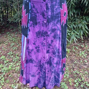 May include: A long purple skirt with a black and red tie-dye pattern. The skirt has a button-up front and a relaxed fit.
