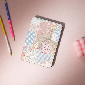 May include: An e-reader cover with a patchwork design featuring a variety of floral and geometric patterns in shades of pink, blue, and white.