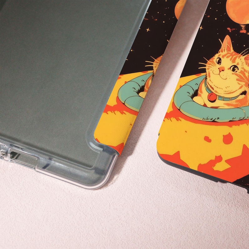 Peut inclure: Un &eacute;tui de t&eacute;l&eacute;phone transparent &agrave; c&ocirc;t&eacute; d'un &eacute;tui de t&eacute;l&eacute;phone avec une illustration color&eacute;e d'un chat en combinaison spatiale. Le chat est orange et blanc, avec un collier bleu et une &eacute;tiquette rouge. Le fond est noir avec des plan&egrave;tes et des &eacute;toiles.