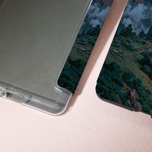 May include: Clear phone case with a landscape design featuring green trees, rocks, and a cloudy sky. The case has a clear, protective border and a printed design on the back.