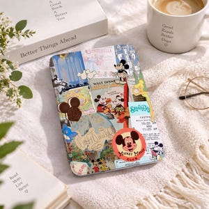 May include: A rectangular e-reader cover featuring a collage of Disney-themed stickers, including Mickey Mouse, Cinderella, Tinker Bell, and a FastPass ticket. The design incorporates various vintage-style illustrations, park maps, and a circular Mickey Mouse Club logo on a light-coloured background.