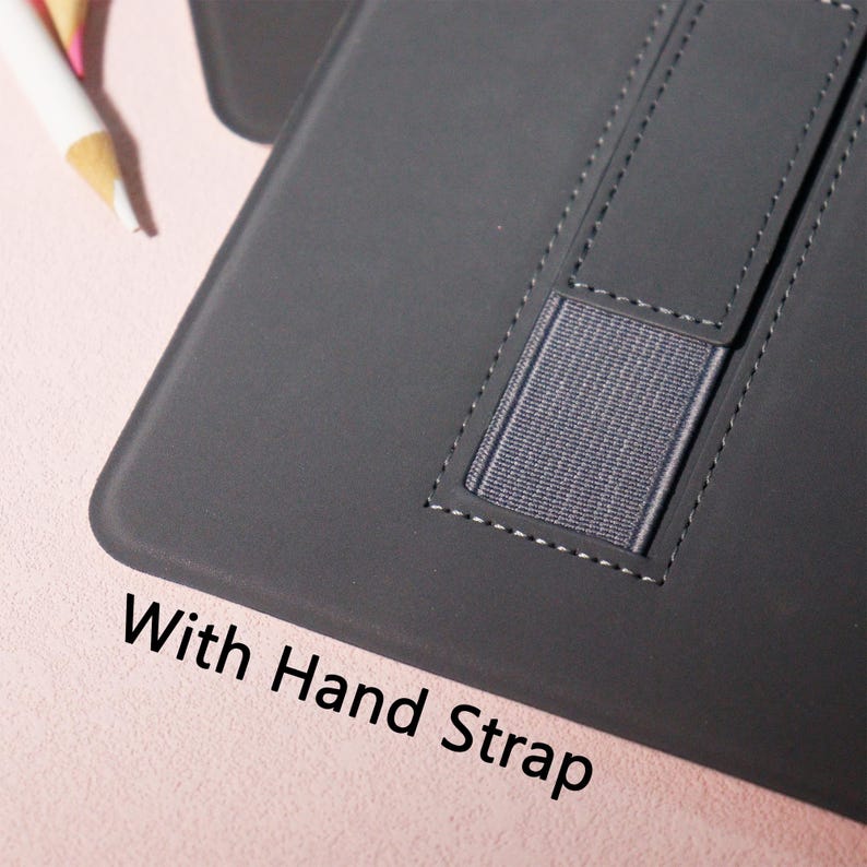 May include: A dark gray tablet case with a hand strap. The case has a stitched design and a gray elastic band for securing the device. The text "With Hand Strap" is printed on the lower left corner.