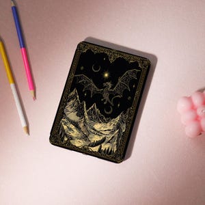 Könnte beinhalten: Schwarze rechteckige Hülle mit einem goldenen Drachen- und Bergdesign. Der Drache fliegt vor einem Nachthimmel mit Sonne, Mond und Sternen. Die Hülle hat einen dekorativen Goldrand.
