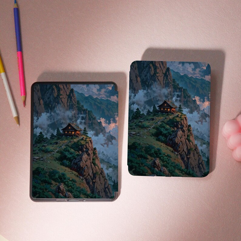May include: Two electronic device cases with a mountain landscape design. The cases feature a small cabin perched on a cliff, surrounded by trees and mountains. The artwork is in shades of green, brown, and blue.