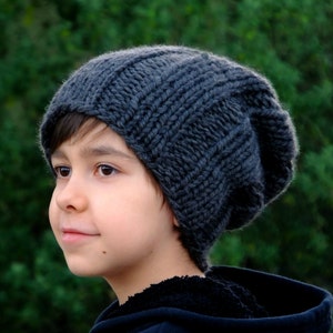 May include: A young person wearing a dark gray slouchy beanie hat. The hat is knitted and has a simple design.