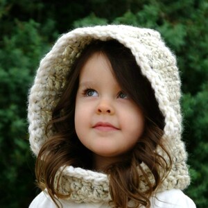 May include: A young girl wearing a white crocheted hooded scarf. The scarf has a textured pattern and is worn over a white shirt.