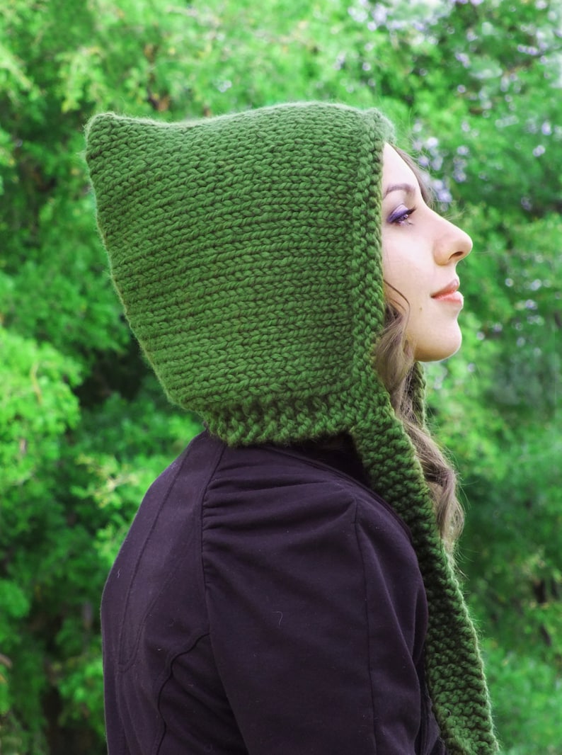 May include: A woman wearing a green knitted hooded scarf. The scarf is long and has a pointed hood. The woman is wearing a black jacket and has long brown hair.